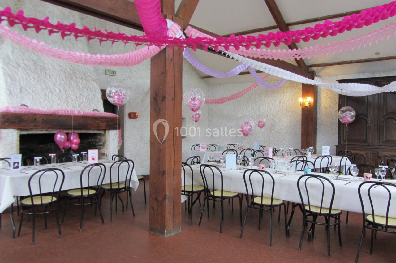 Salle décorée avec des guirlandes roses et blanches, tables dressées pour un événement festif.