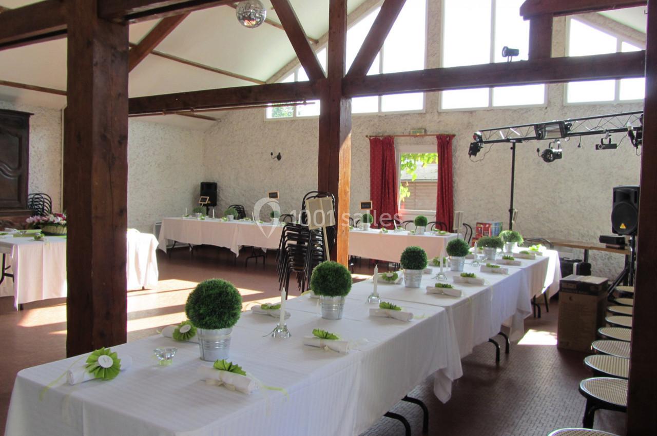 Salle de réception lumineuse avec de longues tables décorées de nappes blanches et de centres de table végétaux.
