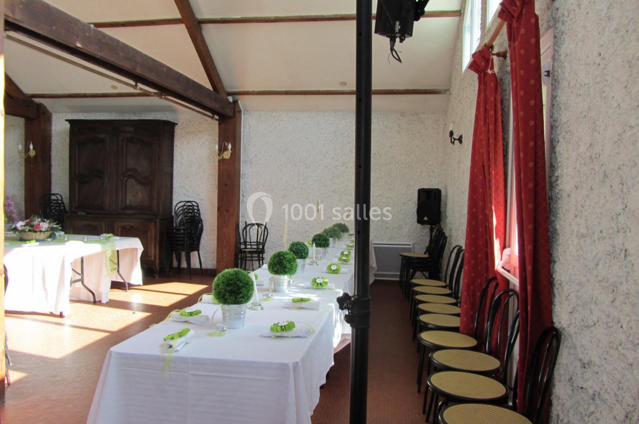 Salle décorée pour un événement avec tables alignées, nappes blanches, centres de table verts et chaises en bois.