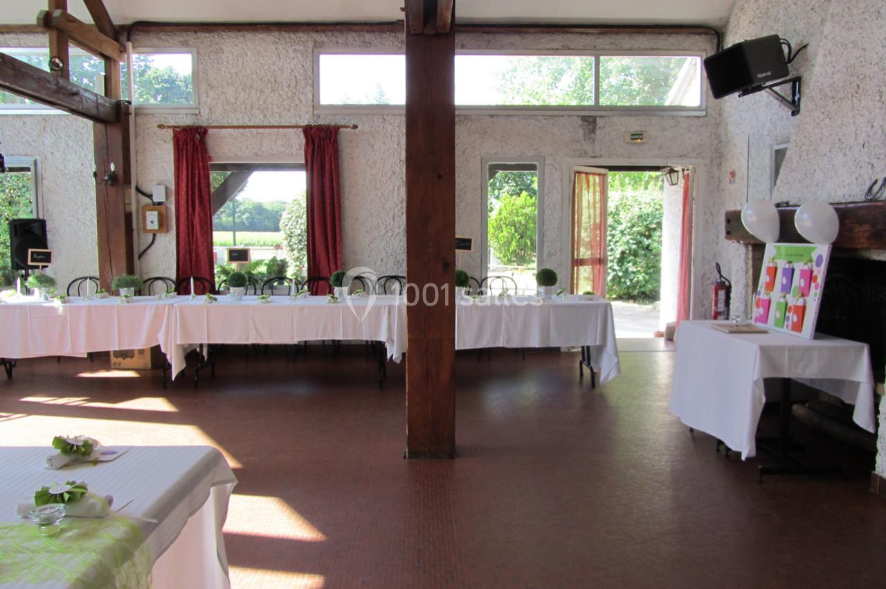 Salle lumineuse avec de grandes fenêtres, tables dressées avec nappes blanches et vue sur un jardin verdoyant.