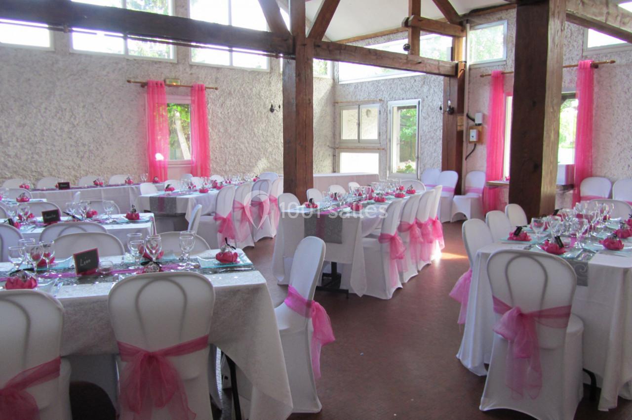 Salle de réception décorée avec des nappes blanches, des chaises ornées de nœuds roses et des tables dressées.