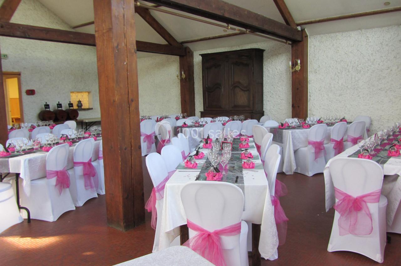 Salle de réception décorée avec des nappes blanches et des chaises ornées de nœuds roses.
