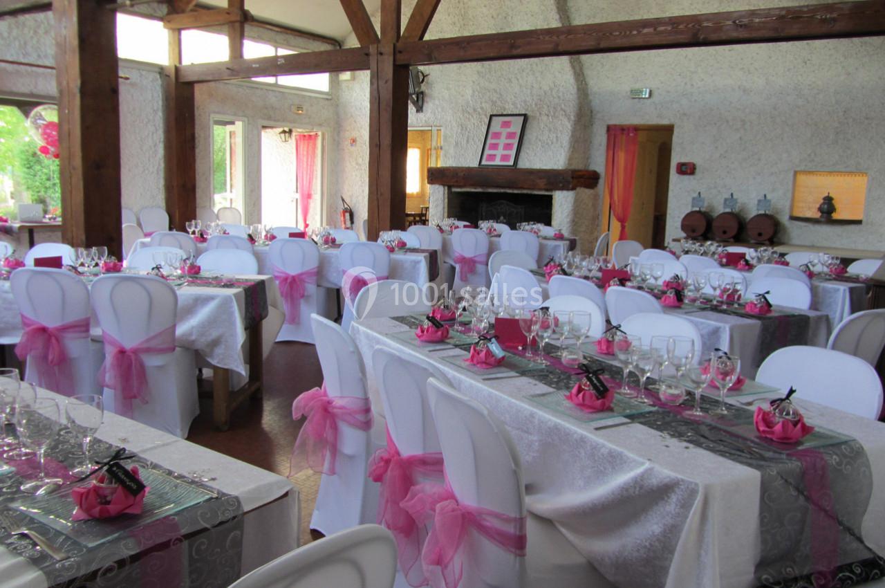 Salle de réception décorée avec des nappes blanches, des rubans roses et des tables dressées pour un événement.