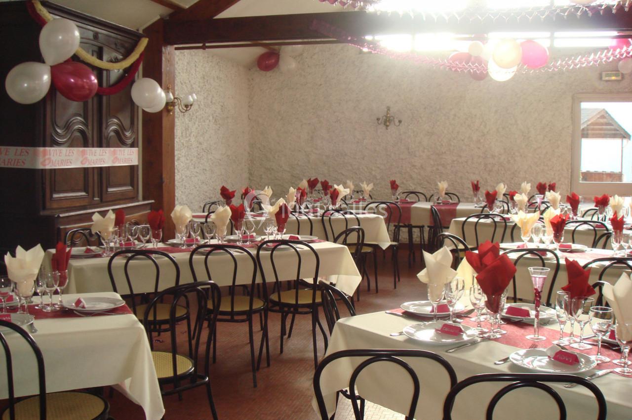 Salle décorée pour un événement avec tables dressées, nappes blanches, serviettes rouges et ballons suspendus.