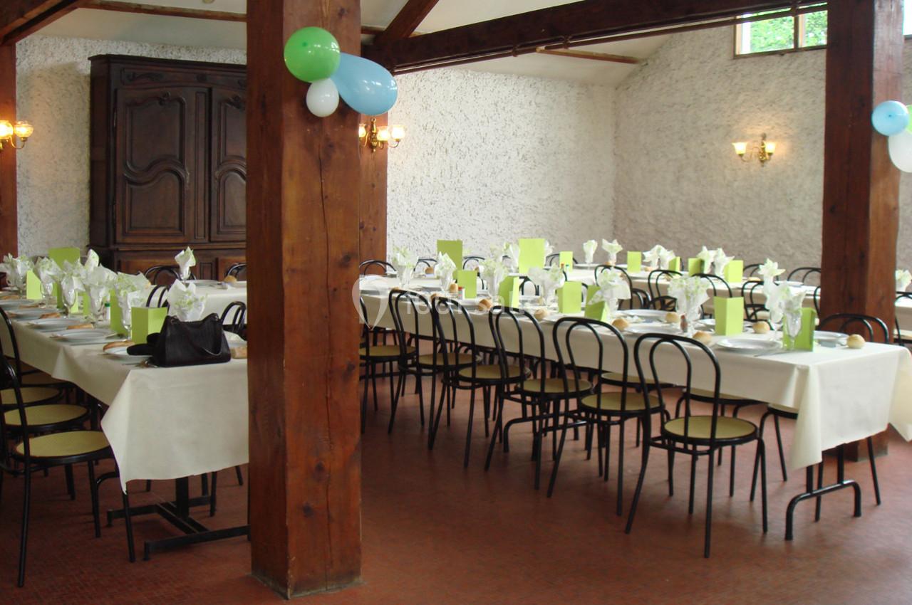 Salle de réception avec tables dressées, nappes blanches, serviettes vertes et chaises noires, décorée de ballons.