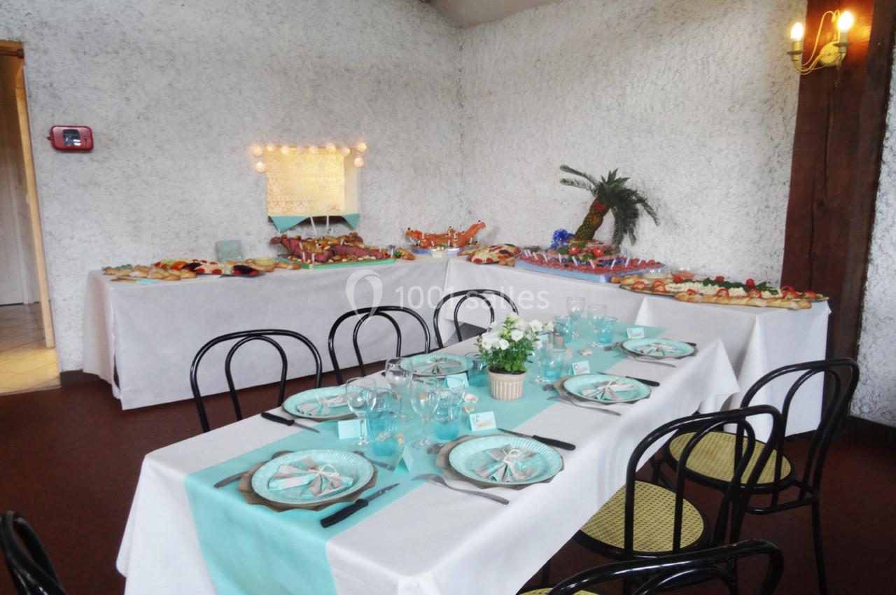 Table dressée avec vaisselle turquoise et buffet garni de plats variés dans une salle au mur blanc texturé.