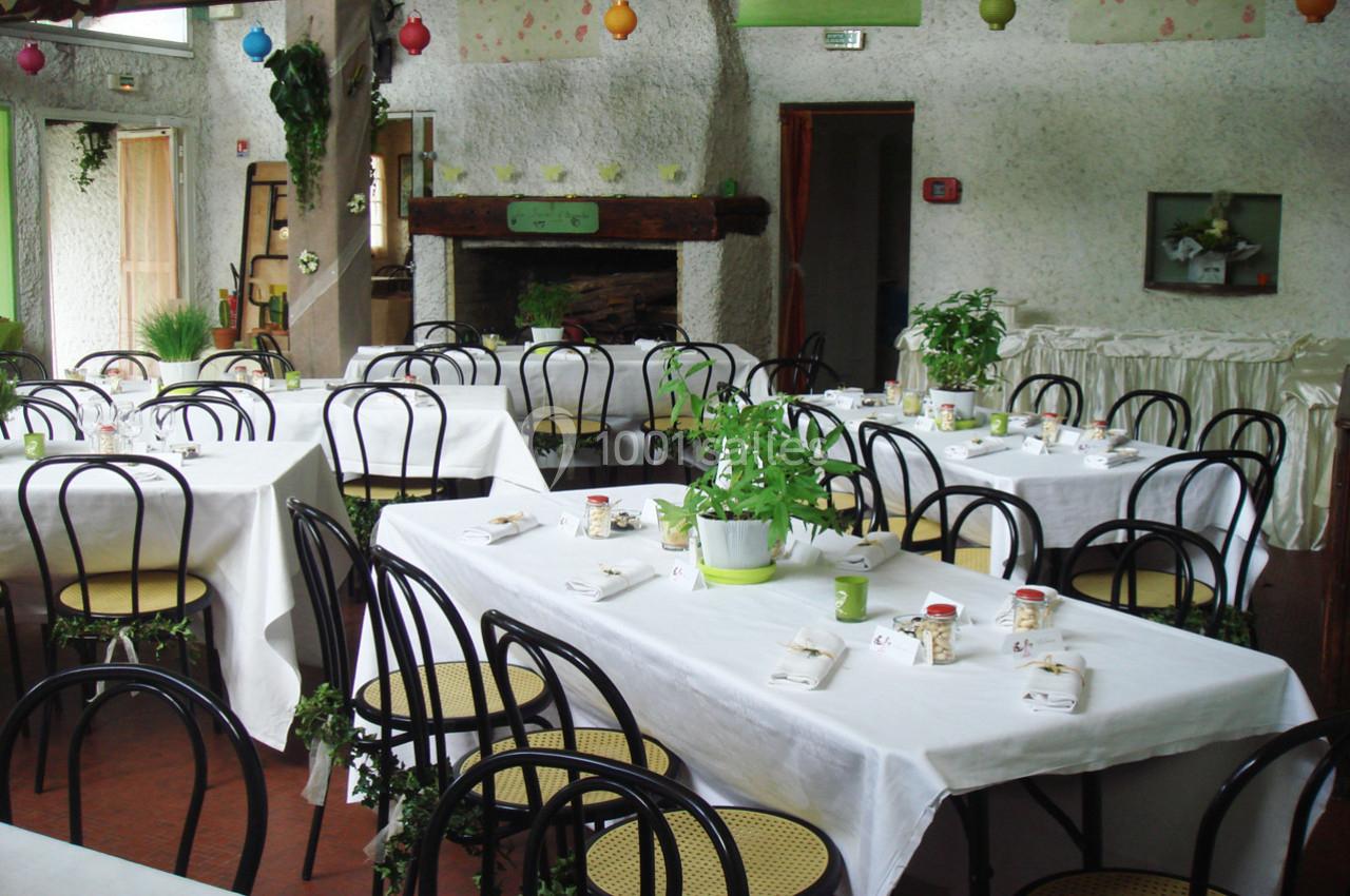 Salle de réception décorée avec des plantes, des nappes blanches et des chaises noires autour de tables dressées.