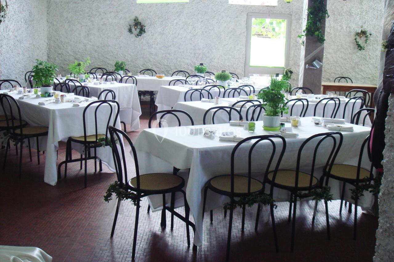 Salle de réception lumineuse avec des tables dressées, nappes blanches et chaises noires, décorée de plantes.