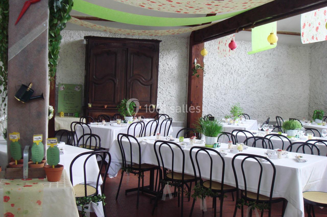 Salle décorée avec des tables dressées, nappes blanches, chaises noires et plantes en pot, ambiance conviviale.