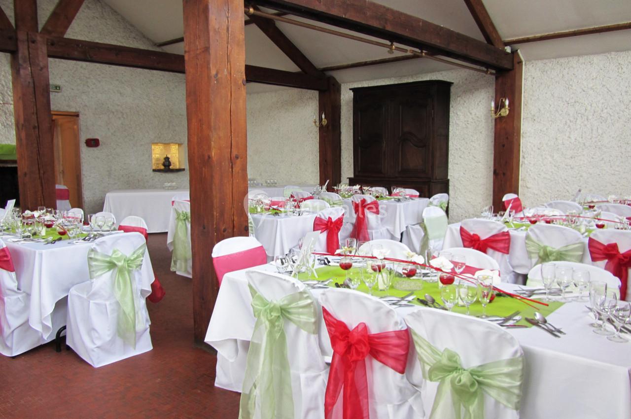 Salle de réception décorée avec des tables dressées, nappes blanches et nœuds de chaises rouges et verts.