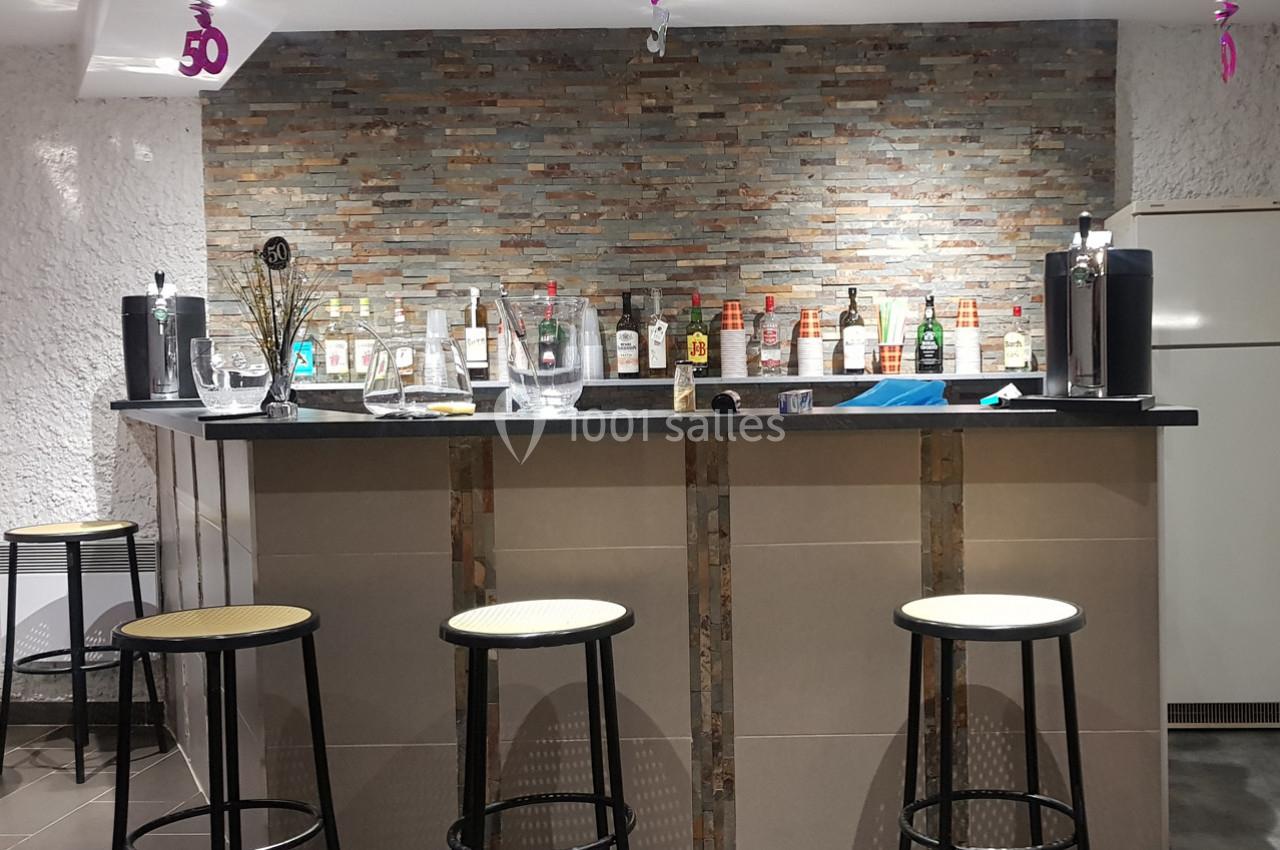 Bar avec comptoir en pierre, tabourets hauts et étagères garnies de bouteilles d'alcool en arrière-plan.