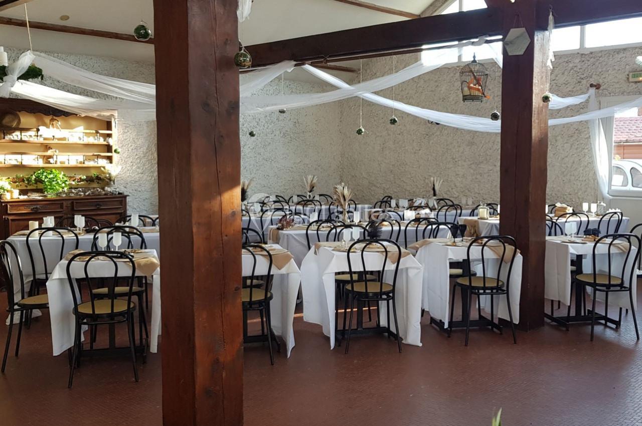 Salle de réception décorée avec des tables rondes nappées de blanc, chaises noires et guirlandes suspendues.