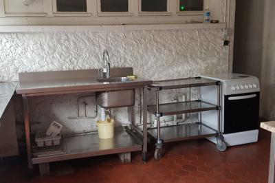 Cuisine simple avec évier en inox, étagères mobiles, cuisinière blanche et sol en carrelage rouge.