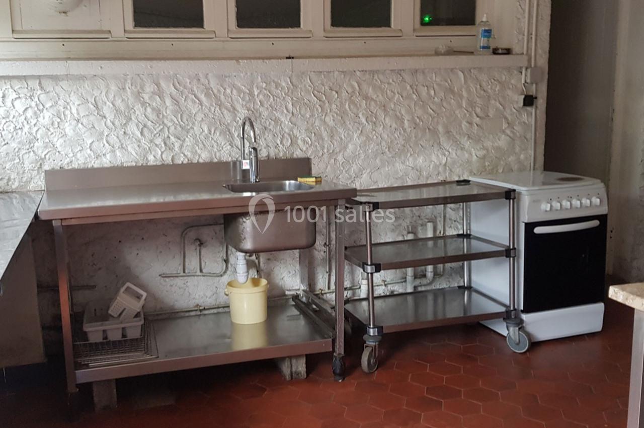 Cuisine simple avec évier en inox, étagères mobiles, cuisinière blanche et sol en carrelage rouge.