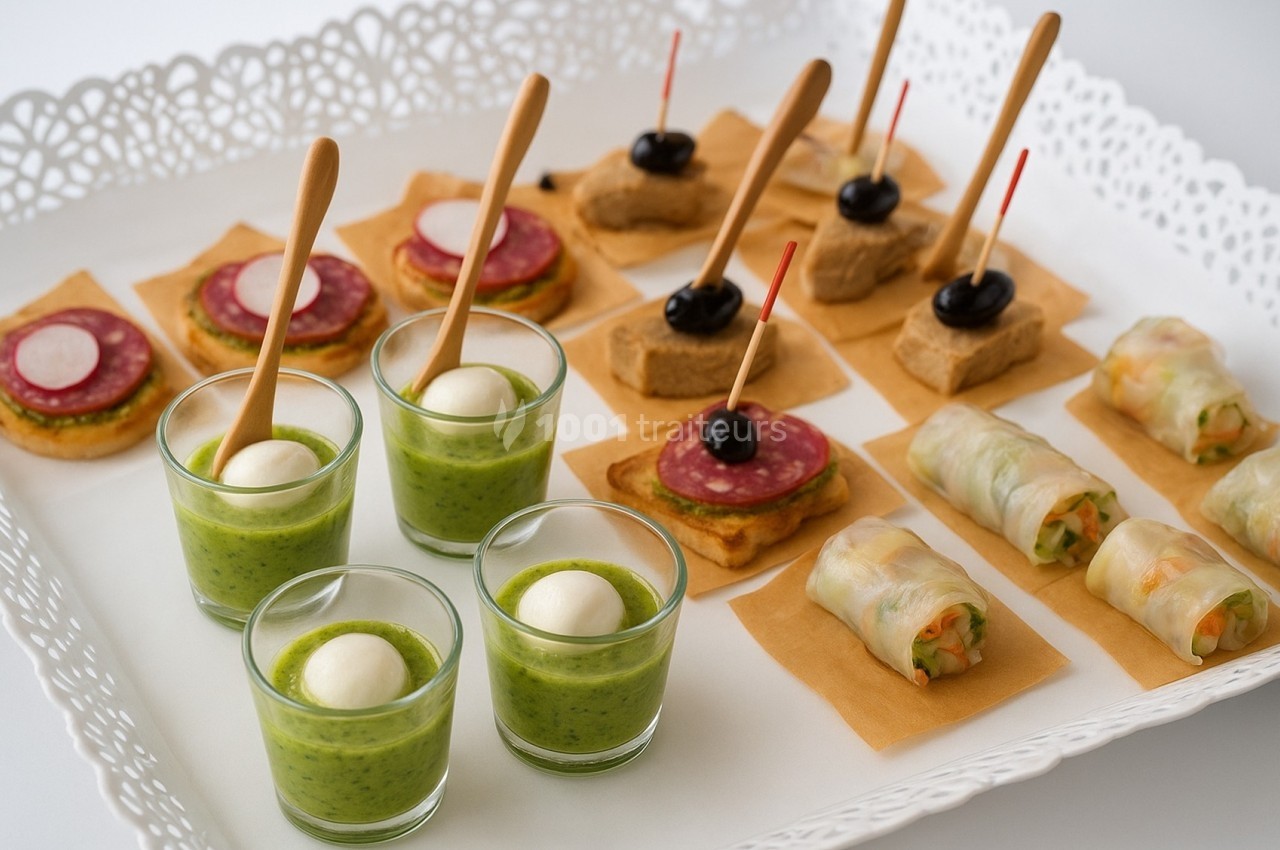 Plateau de bouchées apéritives variées : verrines, roulés de légumes, toasts au salami et canapés aux olives.