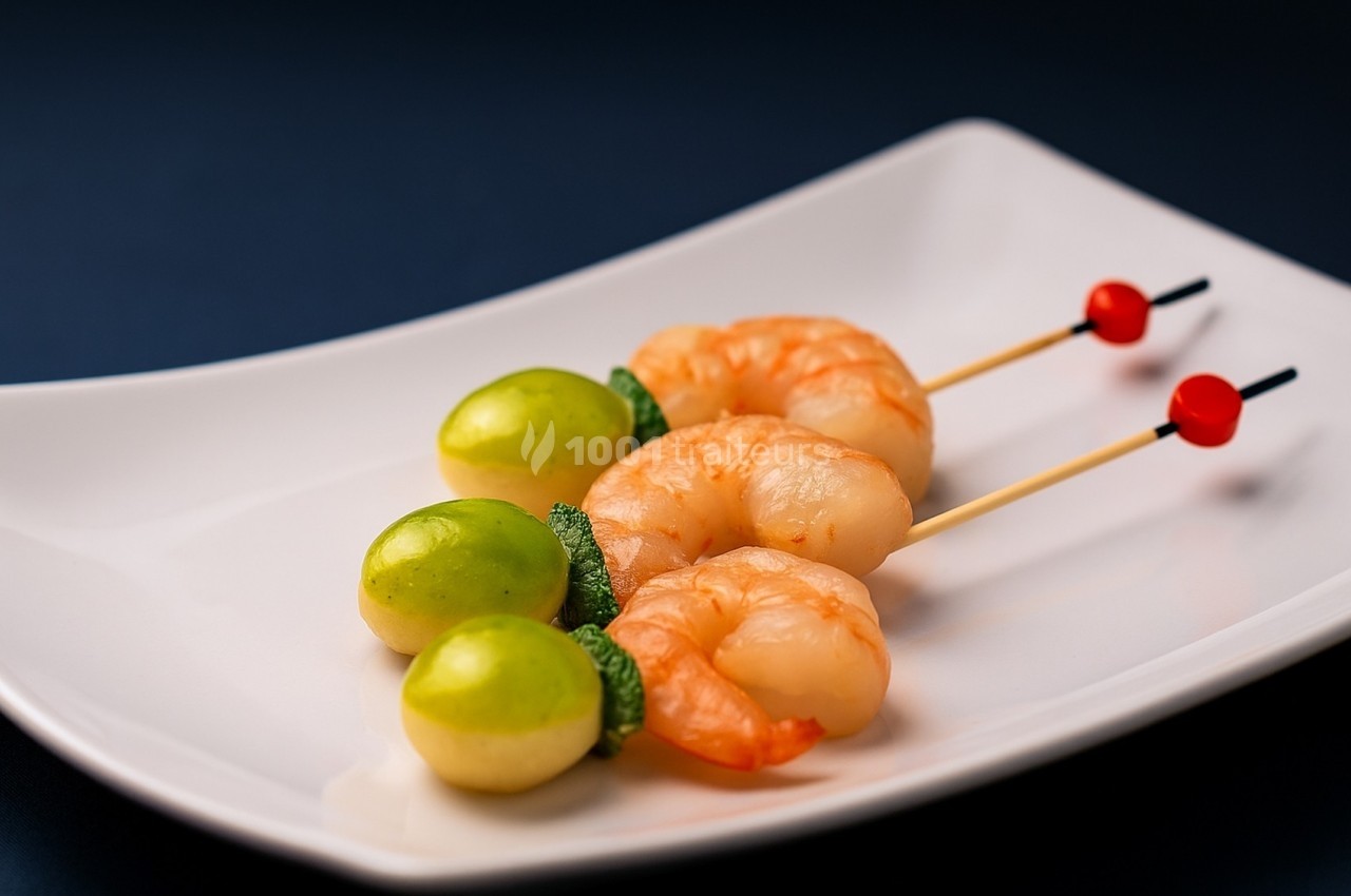 Brochettes de crevettes avec morceaux de pomme verte et feuilles de menthe, présentées sur une assiette blanche.