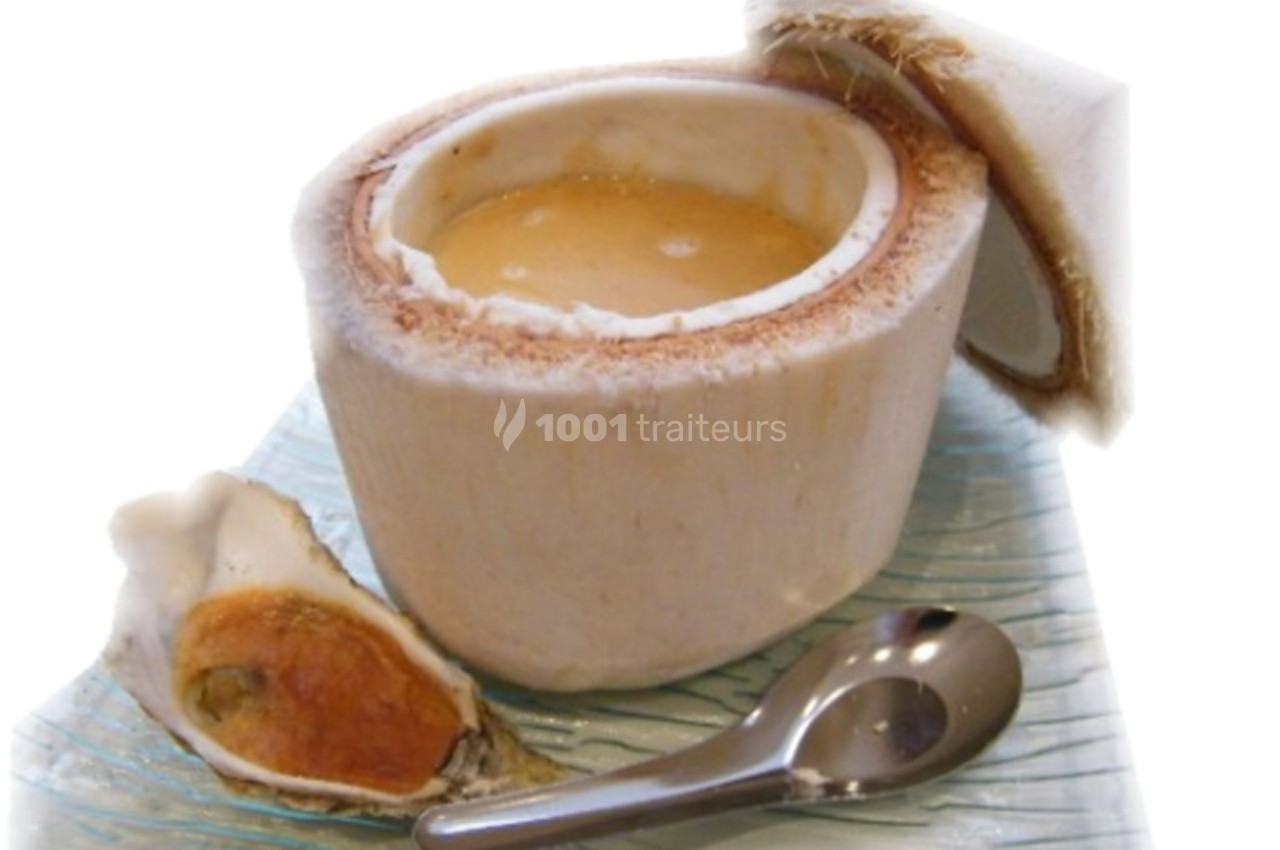 Noix de coco ouverte contenant un liquide, accompagnée d'une huître et d'une cuillère sur une surface texturée.