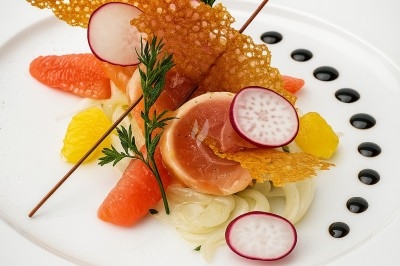 Assiette gastronomique avec tranches de poisson, agrumes, radis, croustillant décoratif et points de sauce balsamique.