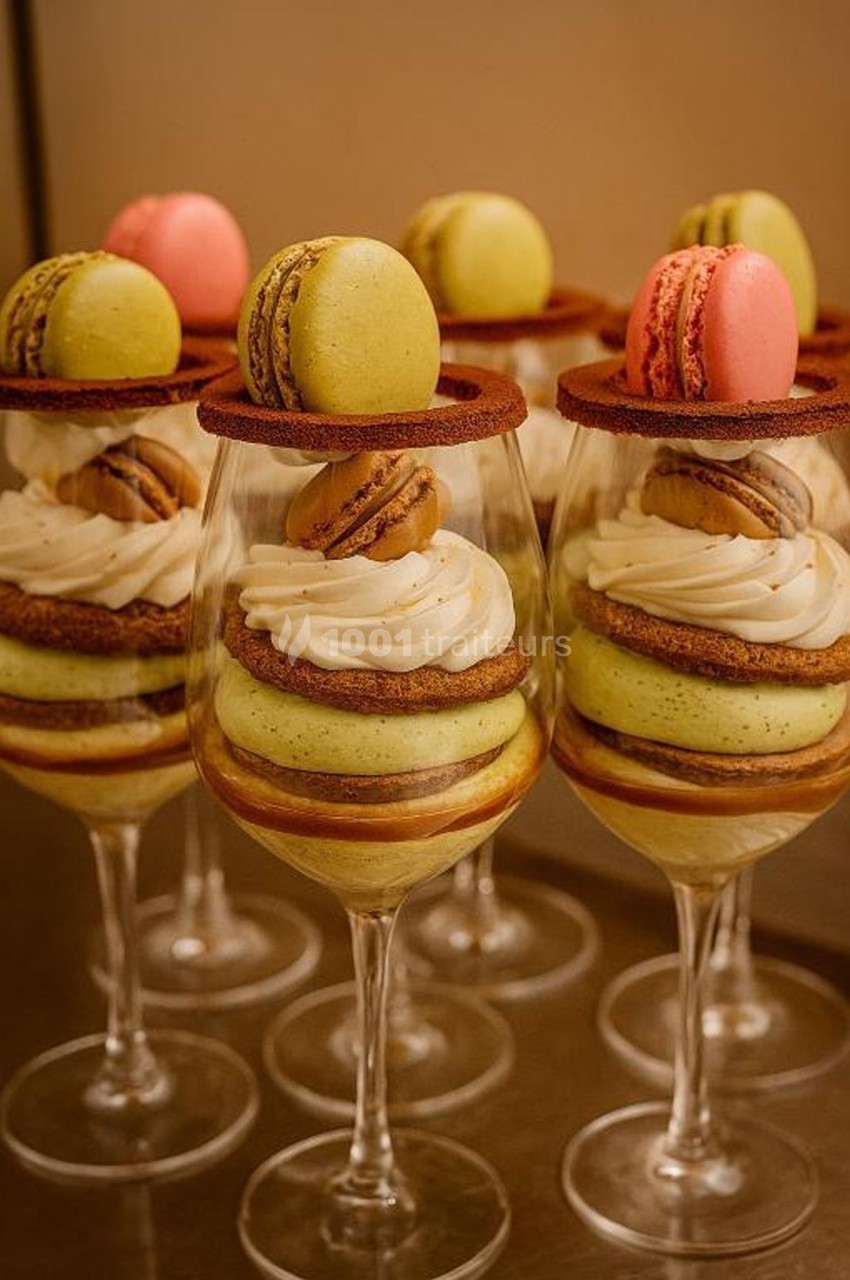 Desserts élégants en verrines, composés de macarons colorés, crème et biscuits, présentés sur une table.