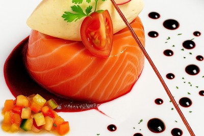 Assiette gastronomique avec tranches de poisson, agrumes, radis, croustillant décoratif et points de sauce balsamique.