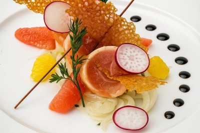 Assiette gastronomique avec tranches de poisson, agrumes, radis, croustillant décoratif et points de sauce balsamique.