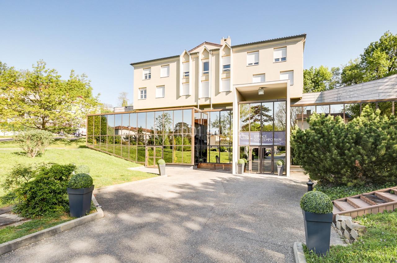 Façade d'un bâtiment moderne avec grandes baies vitrées, entouré de verdure et d'arbustes taillés.