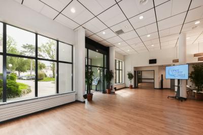 Salle de conférence moderne avec estrade, pupitre transparent, chaises blanches et rangées de sièges vides.