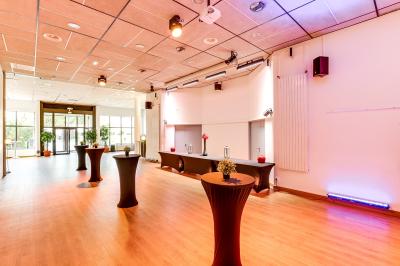 Salle de conférence moderne avec estrade, pupitre transparent, chaises blanches et rangées de sièges vides.