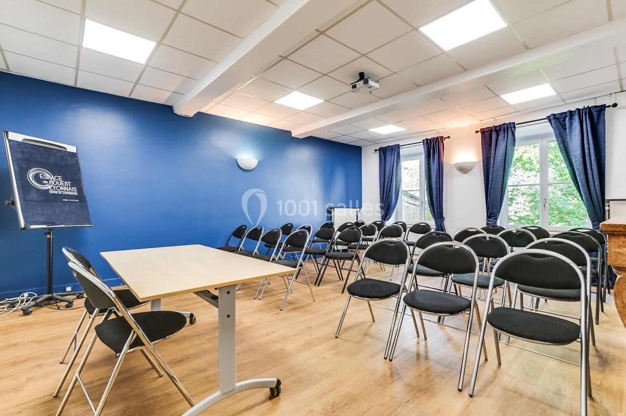 Salle de réunion lumineuse avec murs bleus, chaises noires alignées, tableau de conférence et fenêtres donnant sur des…
