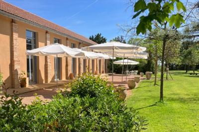 Jardin avec pelouse, arbres et pot en terre cuite au premier plan, éclairé par une lumière douce en fin de journée.
