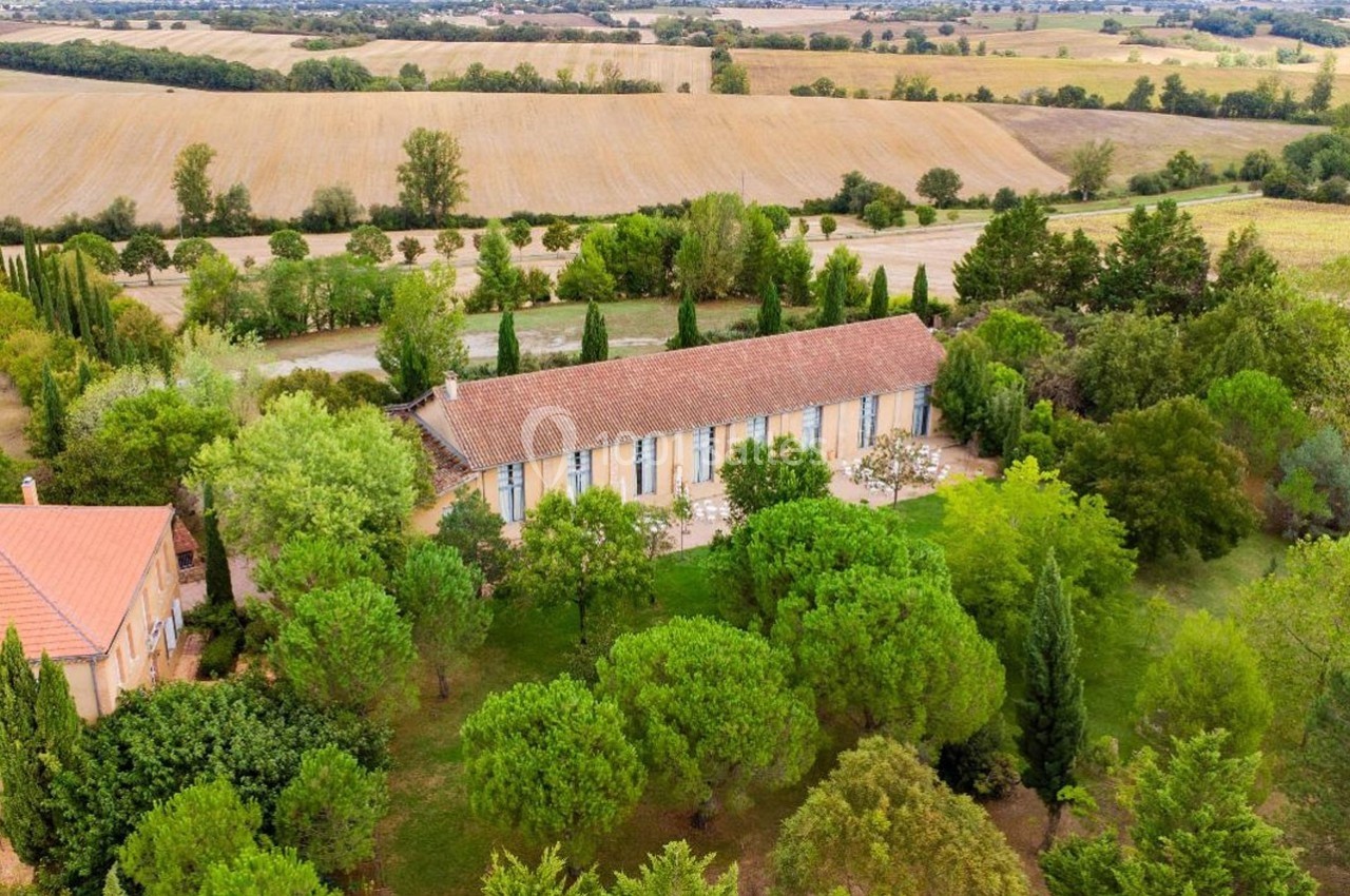 Vue aérienne d'une maison en pierre entourée d'arbres et de champs dans un paysage rural.