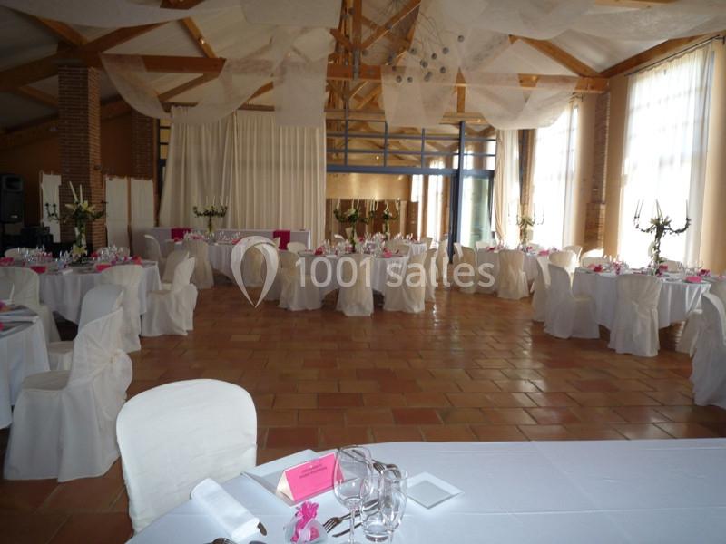Salle de réception décorée avec des tables rondes, nappes blanches et centres de table floraux.