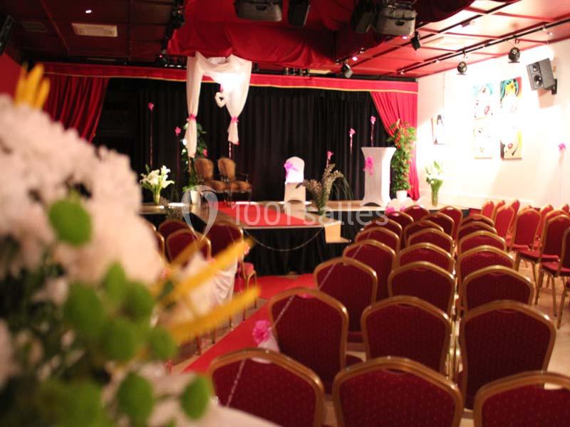 Salle de spectacle décorée avec des chaises rouges, une scène ornée de fleurs et un éclairage tamisé.