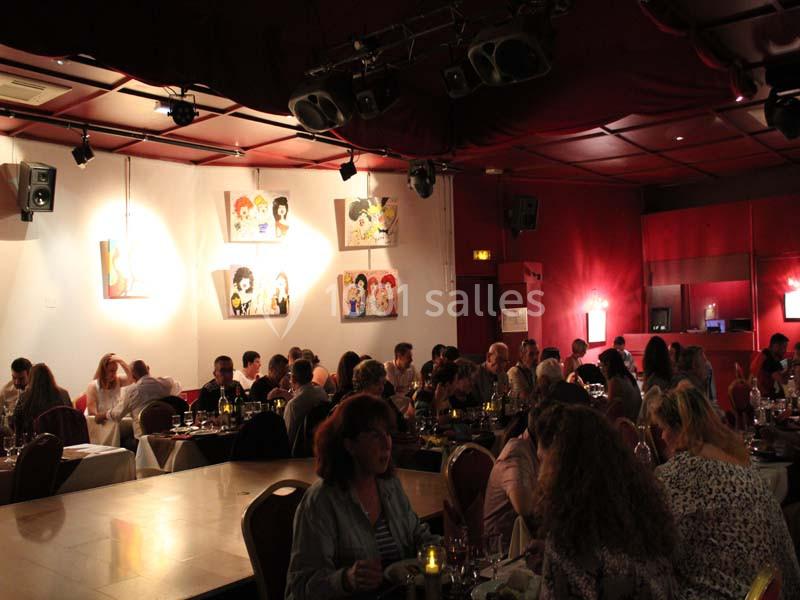 Salle de restaurant animée avec des convives attablés, éclairage tamisé et tableaux colorés accrochés aux murs.