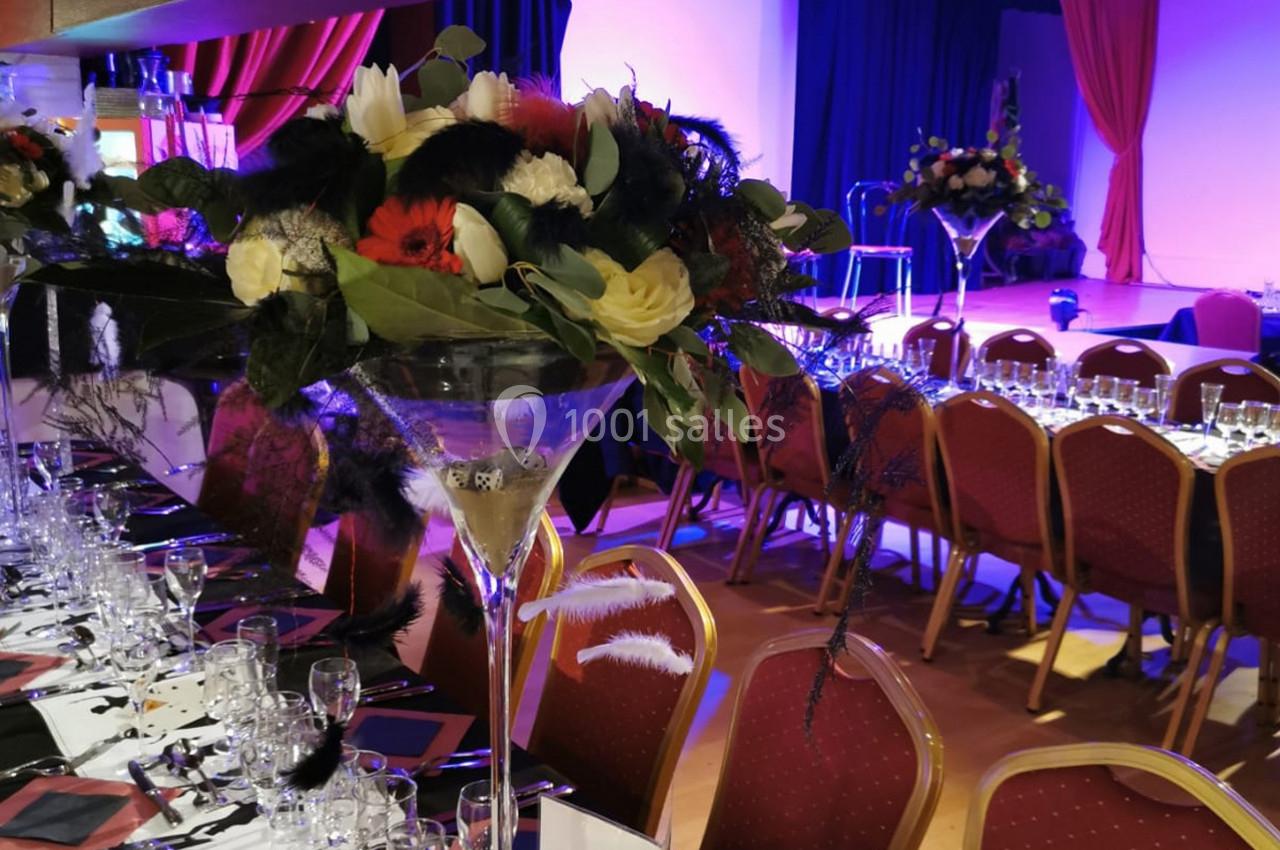 Décoration de table avec des bouquets de fleurs dans des vases hauts, disposée dans une salle de réception éclairée.