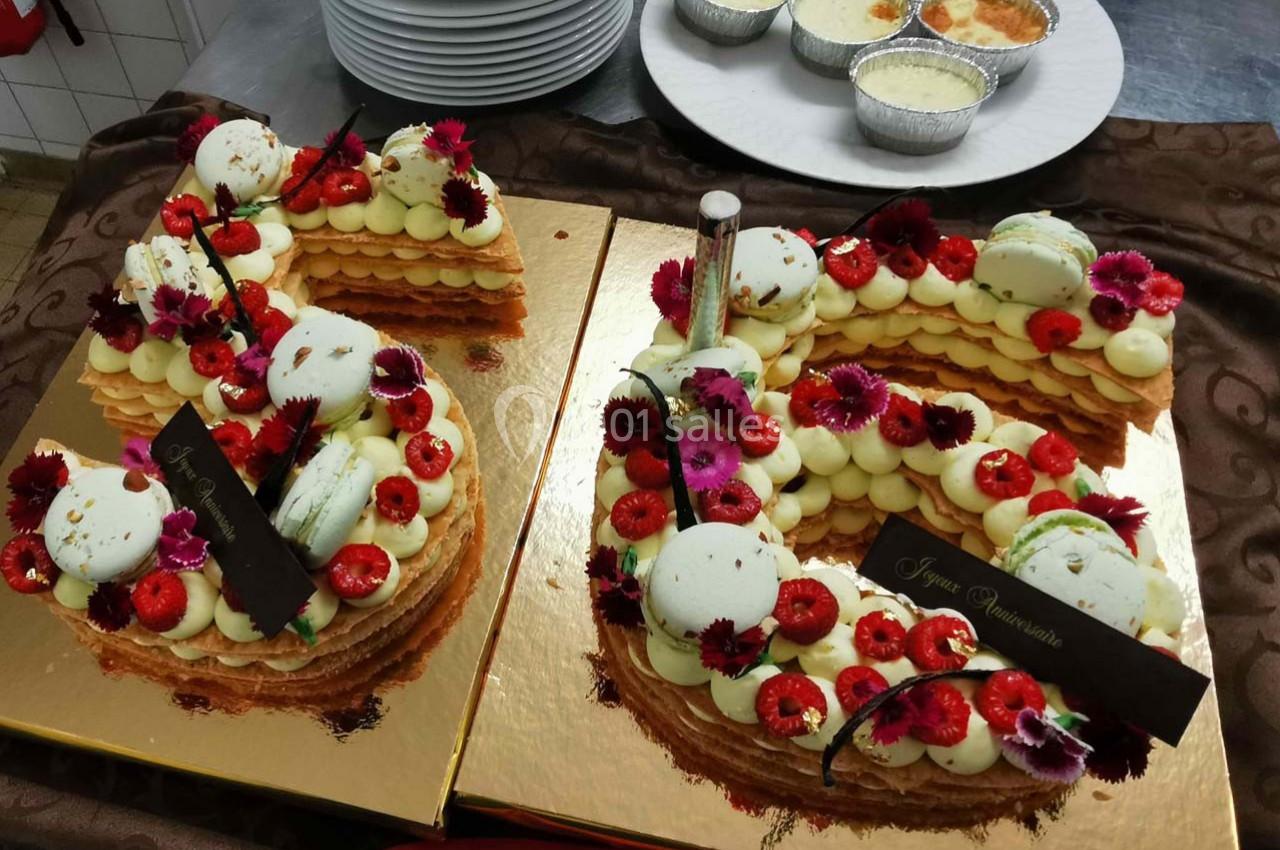 Gâteau en forme de chiffre décoré de fleurs comestibles, macarons et fruits rouges, posé sur un plateau doré.