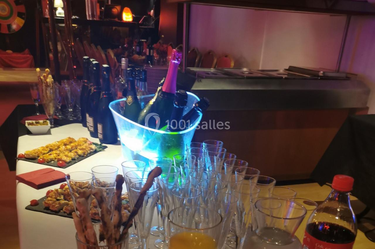 Table dressée avec des verres, une bouteille de champagne dans un seau lumineux, amuse-bouches et boissons variées.