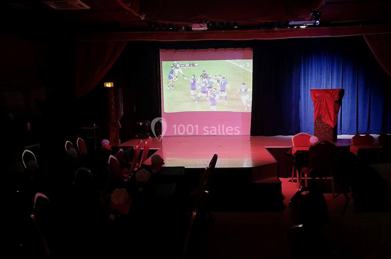 Projection d'un match de football américain sur un écran dans une salle sombre avec des rideaux rouges et bleus.