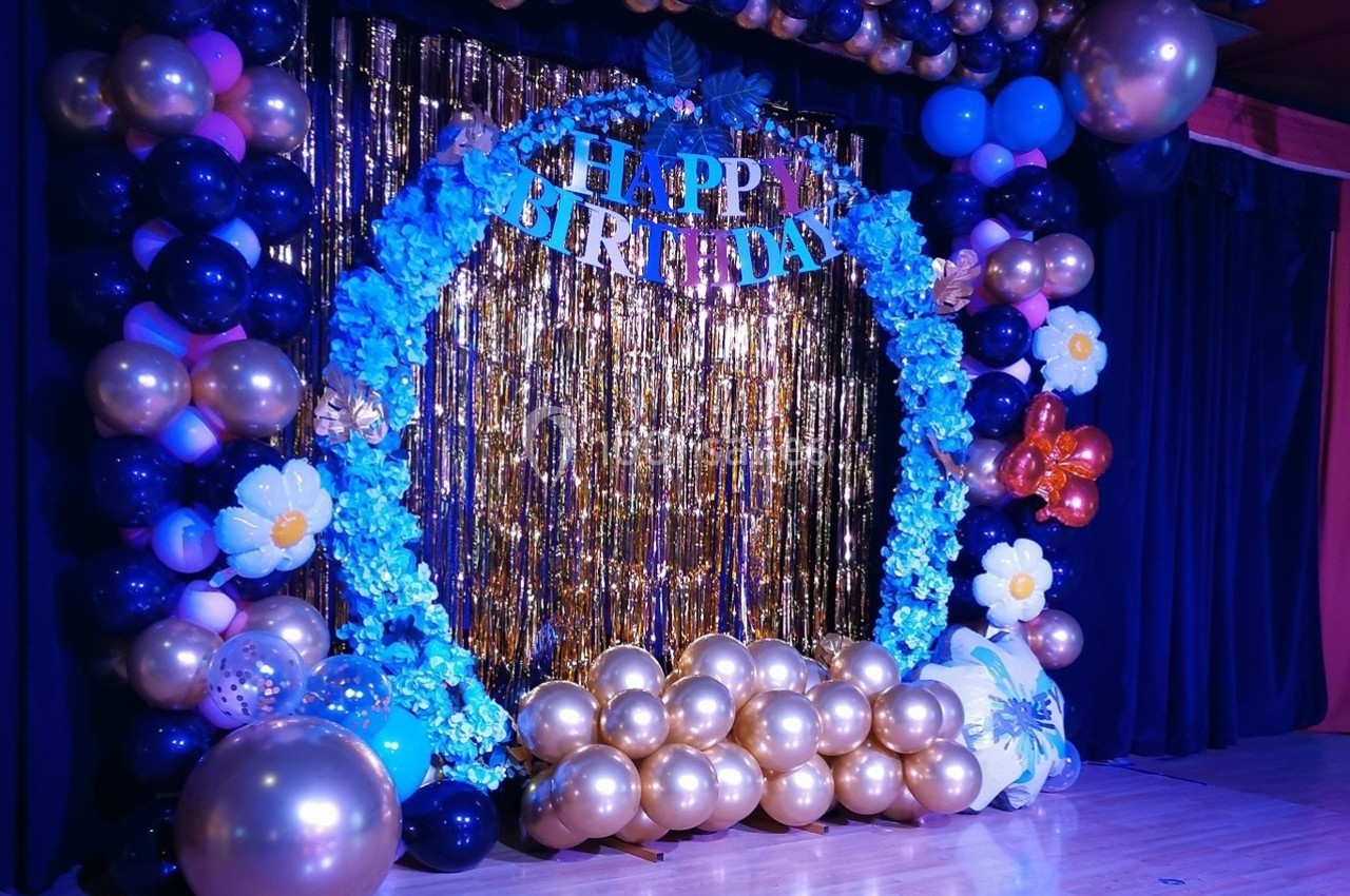 Décor de fête d'anniversaire avec ballons dorés et bleus, guirlandes et rideau scintillant en arrière-plan.