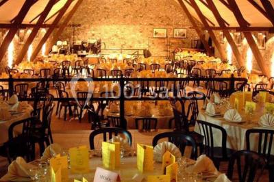 Table dressée avec nappes jaunes, seaux à champagne et verres, sous un grand parasol rouge devant un bâtiment en pierre.