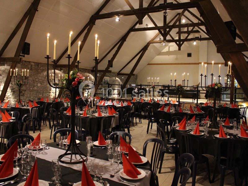 Salle de réception décorée avec des tables dressées, nappes noires, serviettes rouges et chandeliers imposants.