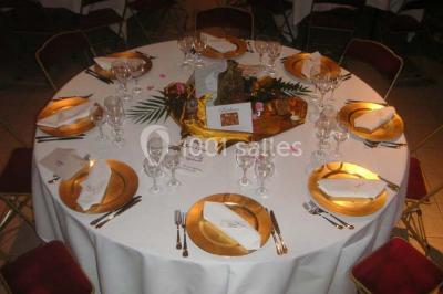 Table dressée avec nappes jaunes, seaux à champagne et verres, sous un grand parasol rouge devant un bâtiment en pierre.
