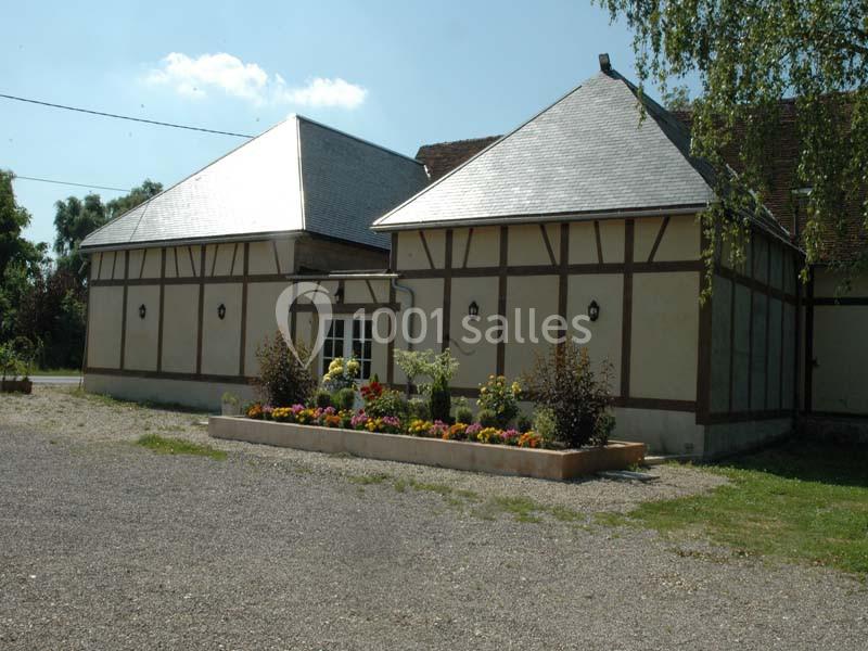 Bâtiment à colombages avec toit en ardoise, parterre fleuri à l'avant et allée gravillonnée au premier plan.