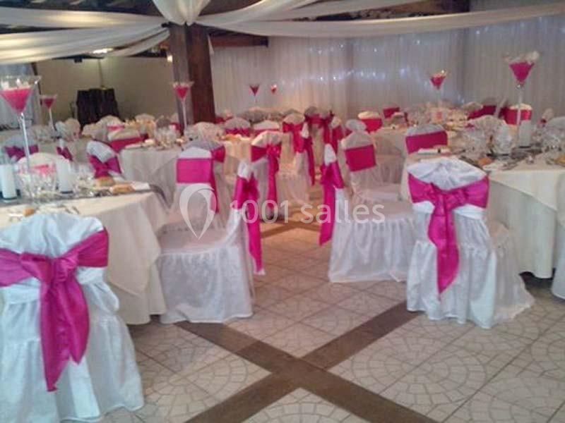 Salle de réception décorée avec des nappes blanches et des chaises ornées de nœuds roses vifs.
