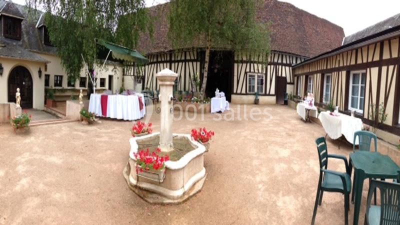 Cour intérieure d'une maison à colombages avec une fontaine centrale, des tables dressées et des chaises disposées autour.
