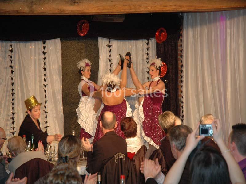 Danseuses en costumes de cabaret exécutant un numéro devant un public attablé dans une salle décorée.