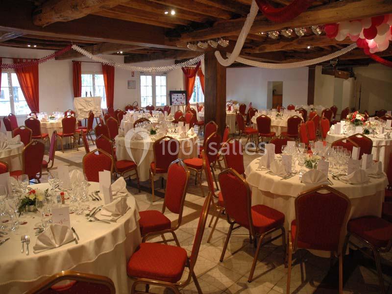 Salle de réception décorée avec des tables rondes dressées, nappes blanches, chaises rouges et guirlandes suspendues.