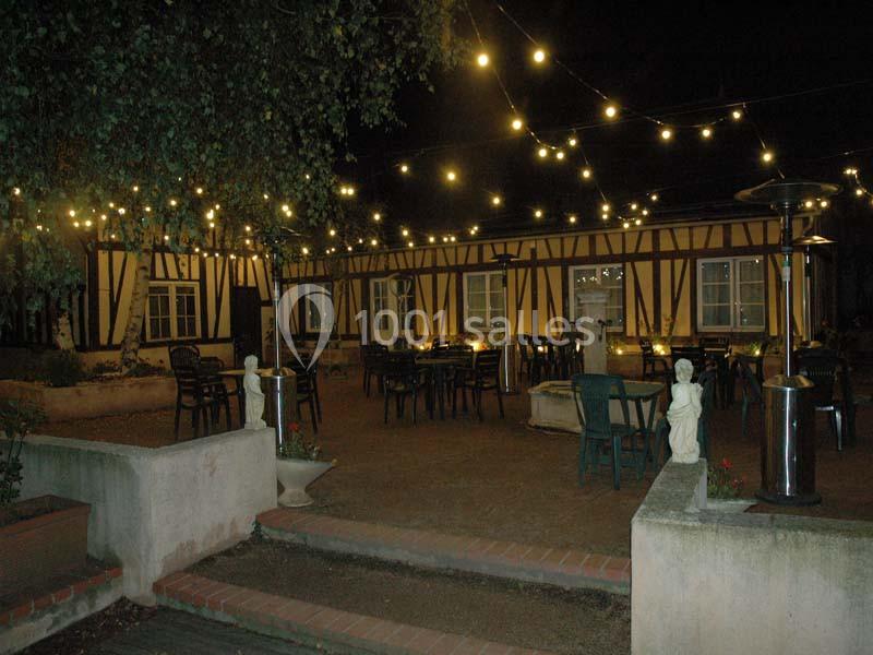 Cour extérieure d'un bâtiment à colombages éclairée par des guirlandes lumineuses, avec des tables et des chaises disposées.