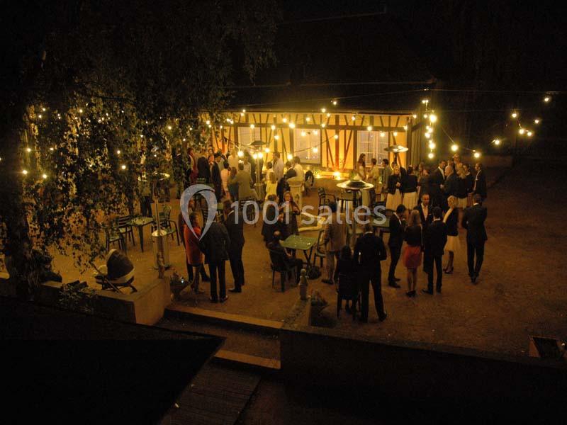 Groupe de personnes rassemblées en soirée dans une cour éclairée par des guirlandes lumineuses.