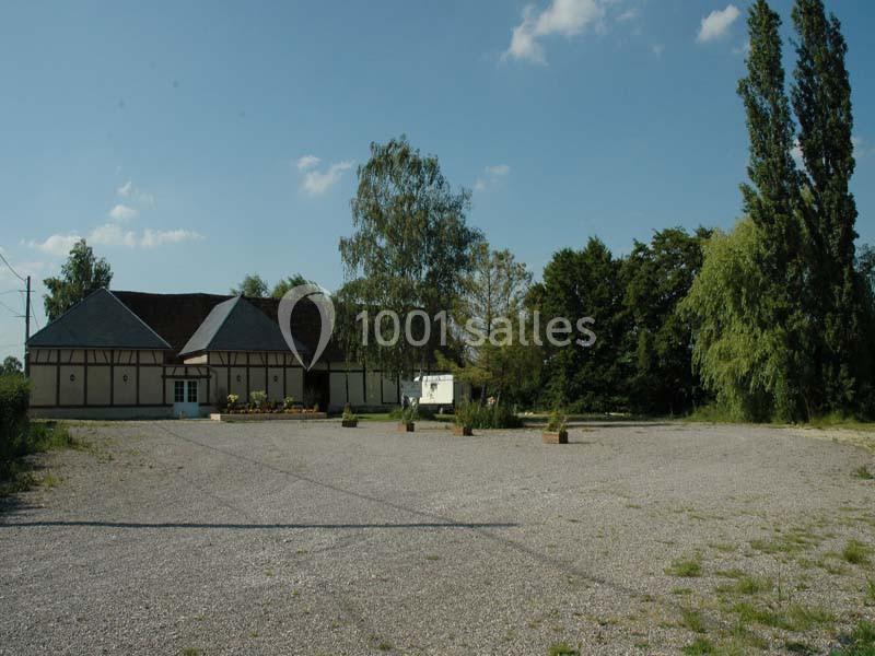 Bâtiment à colombages entouré d'arbres, avec une grande cour en gravier sous un ciel dégagé.